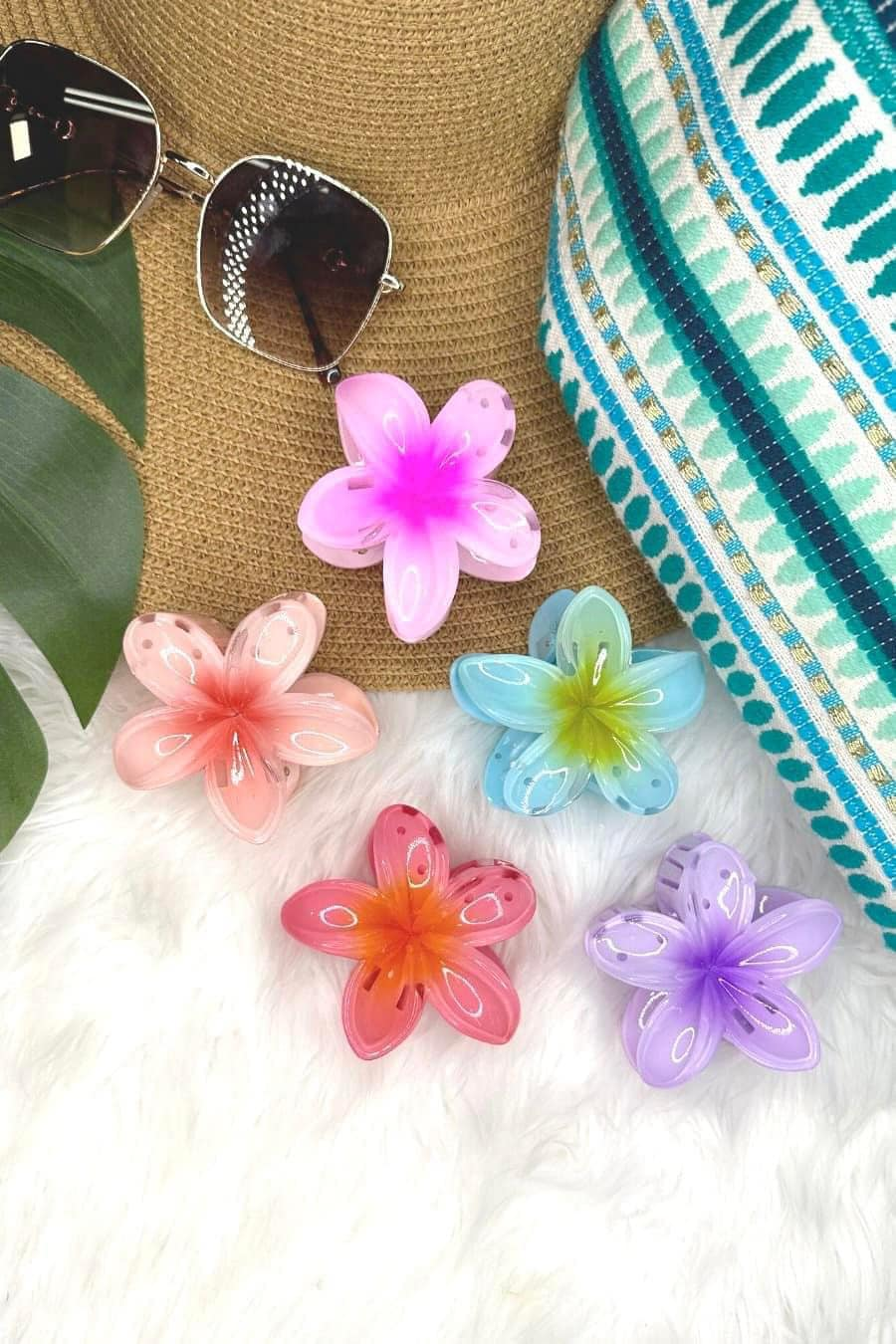 Colorful flower-shaped hair clips on a textured surface with sunglasses and a hat.