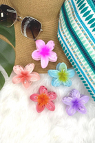 Colorful flower-shaped hair clips on a textured surface with sunglasses and a hat.