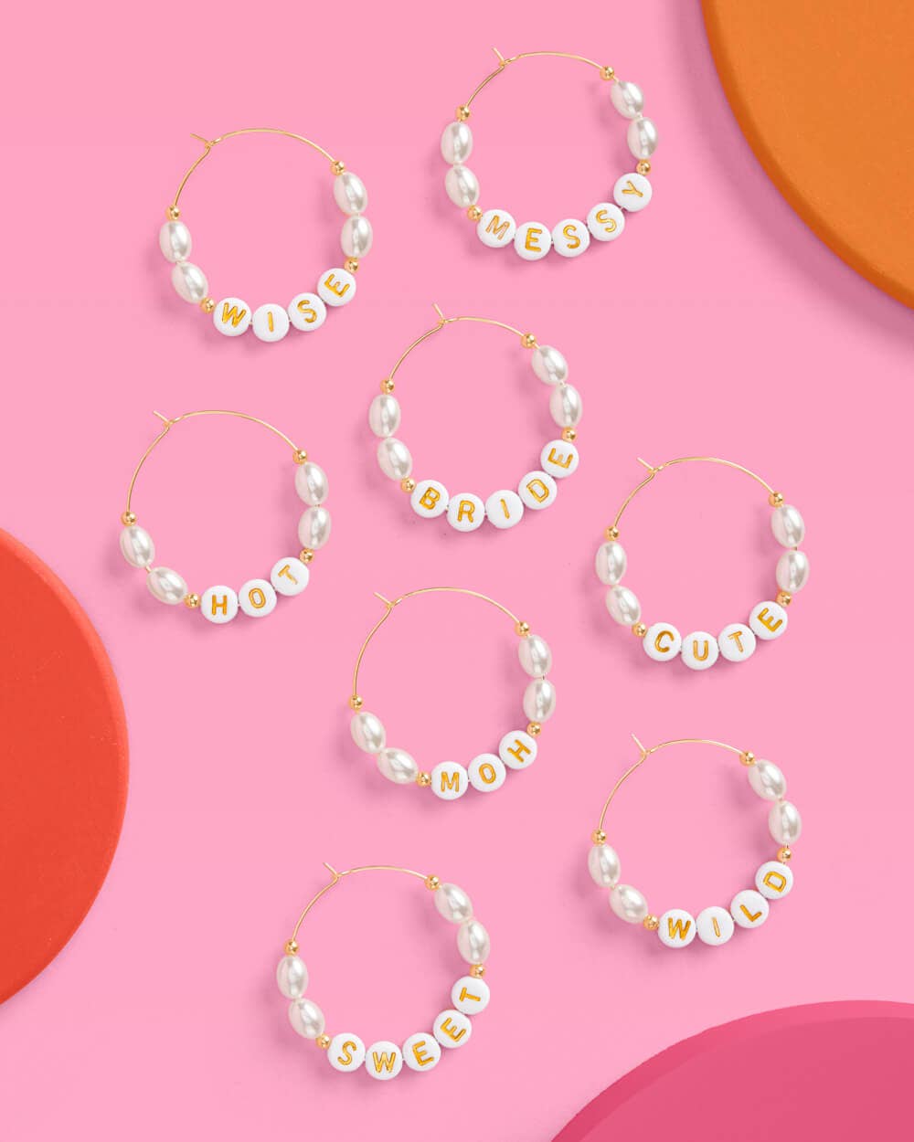 Set of pearl hoop earrings with personalized name charms on a pink background