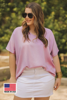 a lightweight lilac short-sleeve woven tunic with a V-neckline, a front chest pocket, and a relaxed, non-stretch silhouette, accented with a MADE IN USA watermark in the bottom left-hand corner 