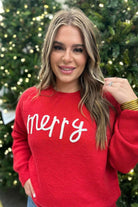 a red long-sleeve patterned sweater adorned with 'merry' script across the chest in white and ribbed detailing at the cuffs, neckline, and hem