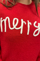 a red long-sleeve patterned sweater adorned with 'merry' script across the chest in white and ribbed detailing at the cuffs, neckline, and hem
