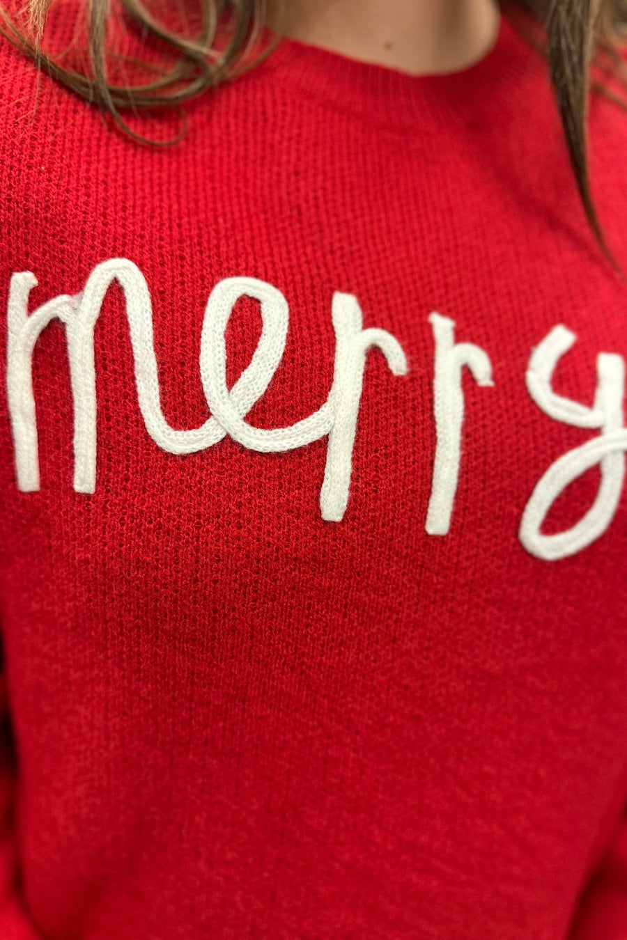 a red long-sleeve patterned sweater adorned with 'merry' script across the chest in white and ribbed detailing at the cuffs, neckline, and hem