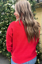 a red long-sleeve patterned sweater adorned with 'merry' script across the chest in white and ribbed detailing at the cuffs, neckline, and hem