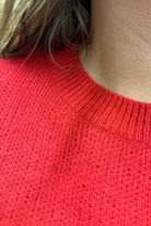 a red long-sleeve patterned sweater adorned with 'merry' script across the chest in white and ribbed detailing at the cuffs, neckline, and hem