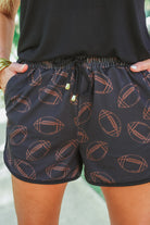 mid-rise relaxed fit activewear shorts with side pockets and a tie waist drawstring with gold bead accents, designed on an all-over football outline pattern print fabric, black base, and black trim