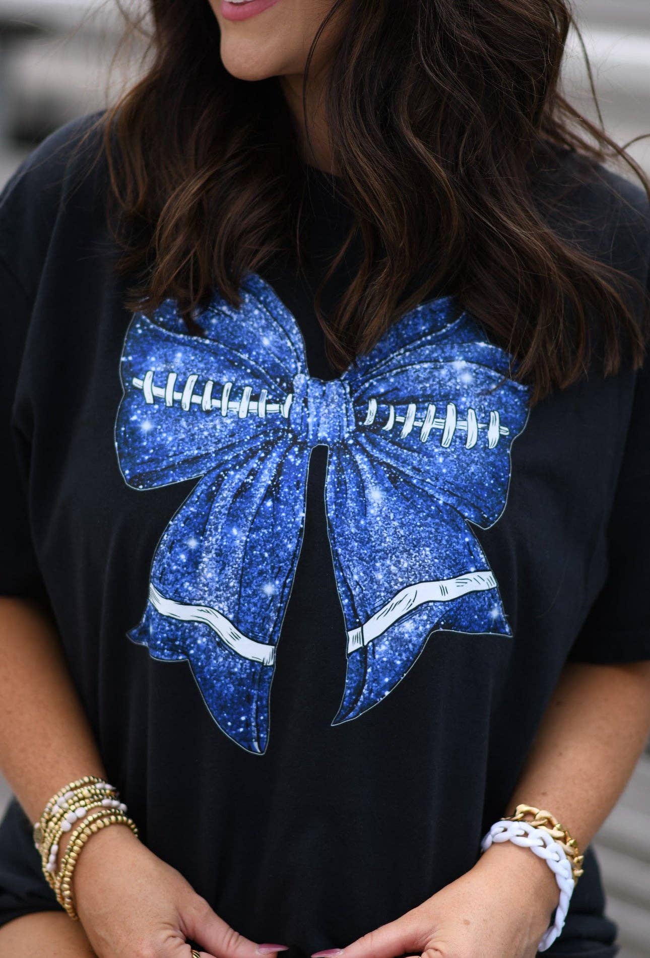 a black Comfort Colors tee crafted on soft garment-dyed cotton with a DTF-printed blue faux glitter football bow graphic, crew neckline, and short sleeves in both youth and adult sizing