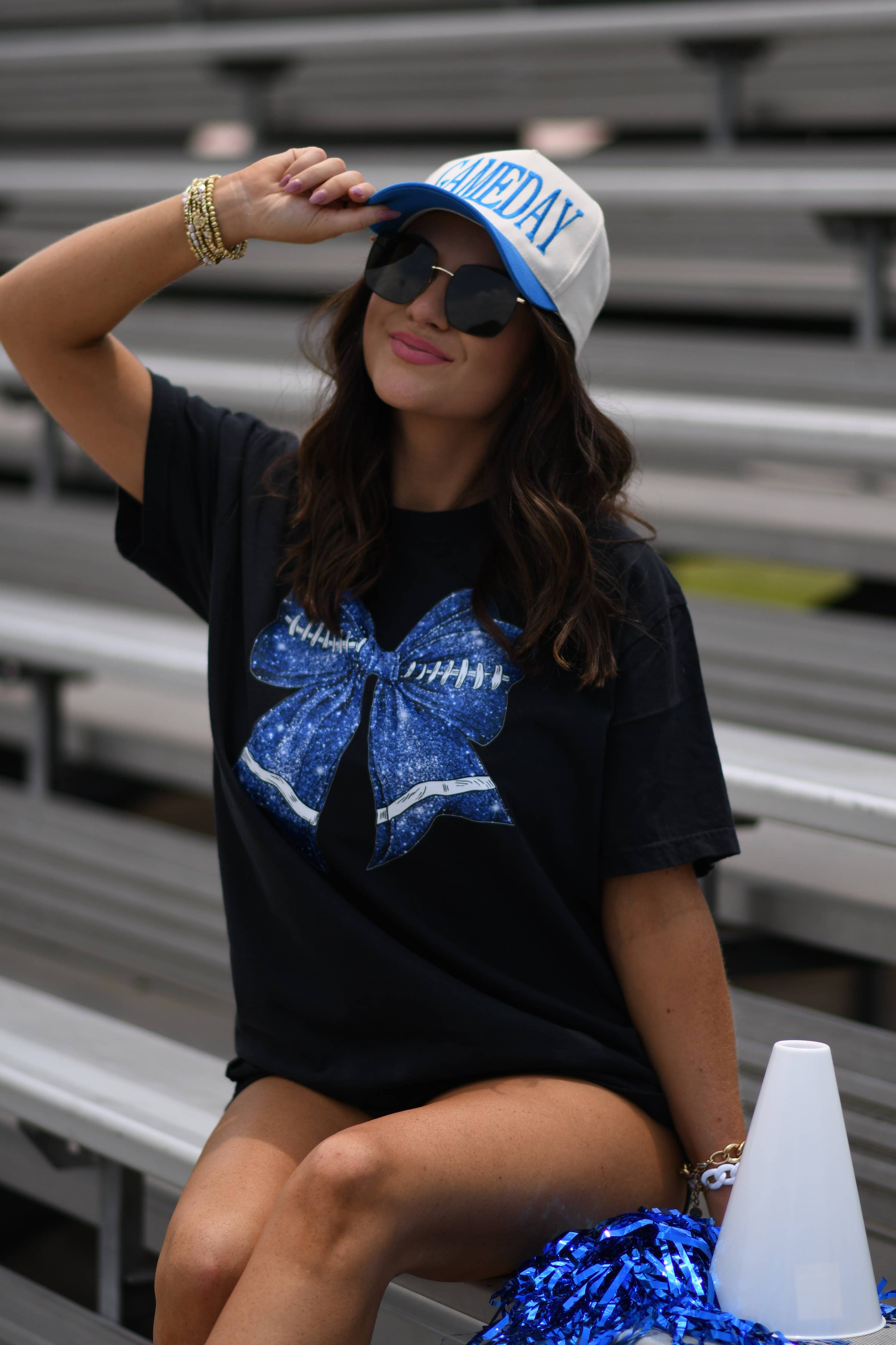 a black Comfort Colors tee crafted on soft garment-dyed cotton with a DTF-printed blue faux glitter football bow graphic, crew neckline, and short sleeves in both youth and adult sizing