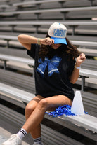a black Comfort Colors tee crafted on soft garment-dyed cotton with a DTF-printed blue faux glitter football bow graphic, crew neckline, and short sleeves in both youth and adult sizing