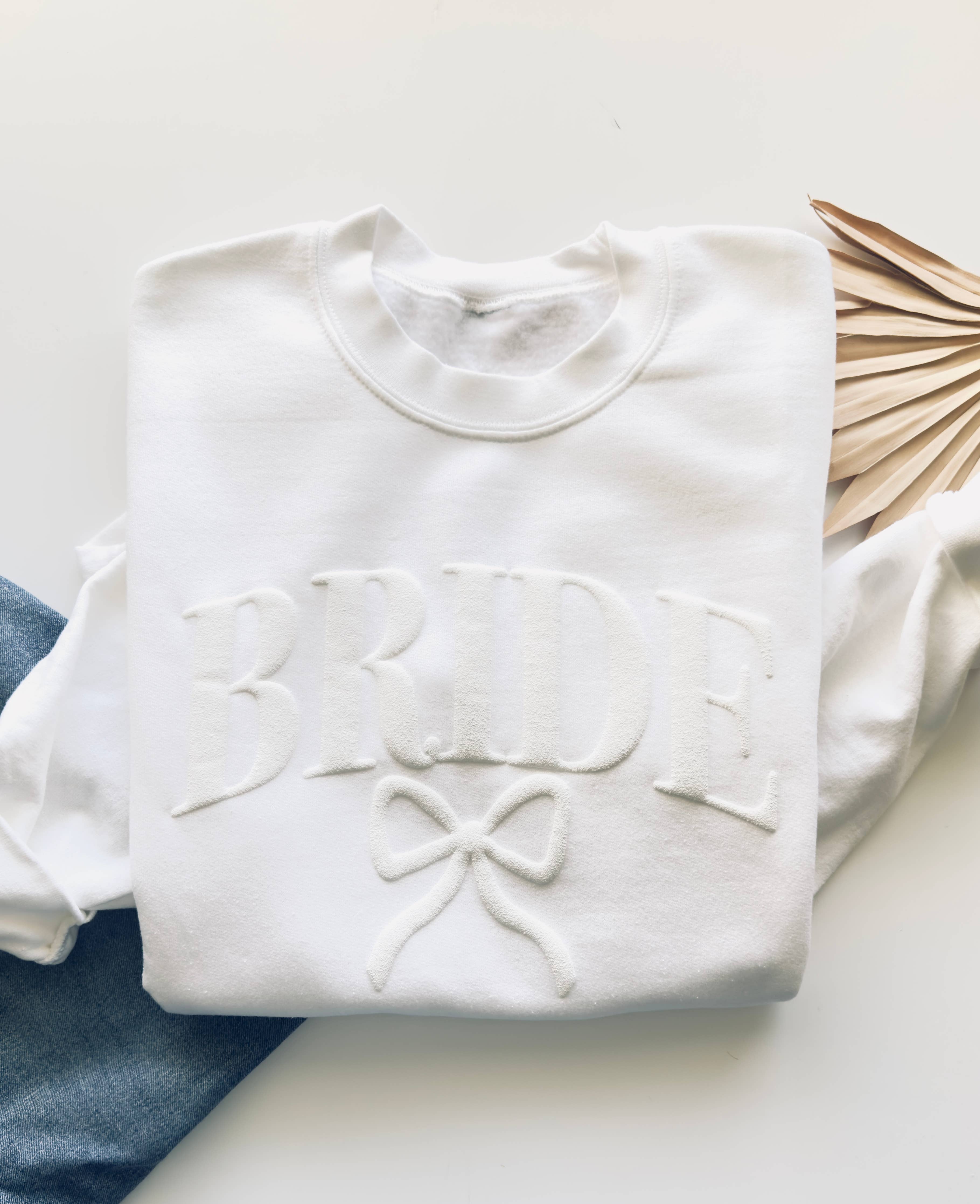 White sweatshirt with 'Bride' and bow design on a white surface
