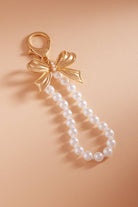 Pearl keychain with a gold bow charm on a beige background