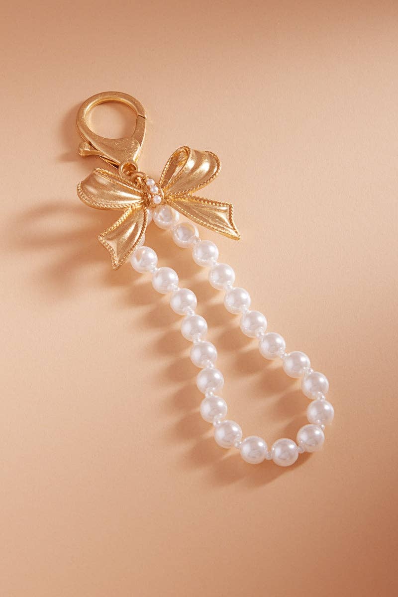Pearl keychain with a gold bow charm on a beige background