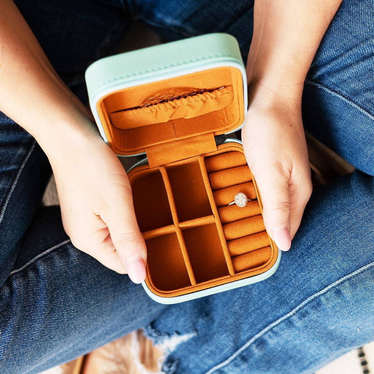 Person holding an open jewelry case with a ring inside, wearing blue jeans.