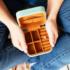 Person holding an open jewelry case with a ring inside, wearing blue jeans.