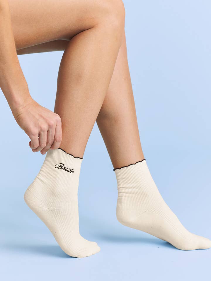 Person wearing white socks with 'Bride' text on a light blue background