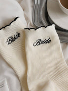 White socks with 'Bride' embroidery on a table setting with plates and a cup.