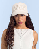 Woman wearing a beige 'BRIDE' cap against a light blue background