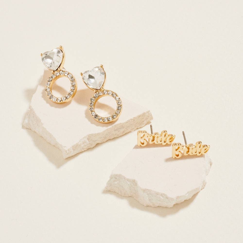 Gold earrings with clear stones on a textured beige surface