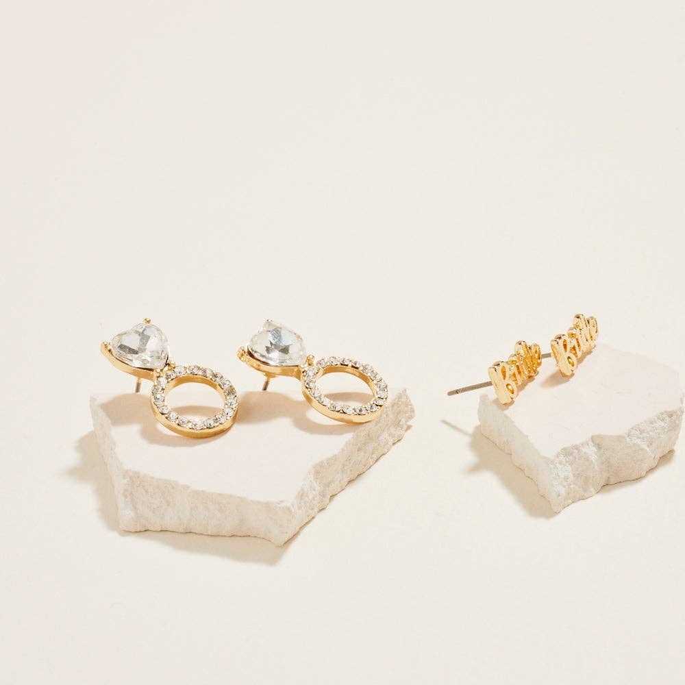 Gold hoop earrings with clear gemstones on a textured beige surface