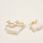Gold hoop earrings with clear gemstones on a textured beige surface