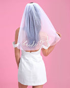 Person wearing a 'bride to be' veil against a pink background