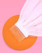 White hair dye brush on an orange circle with a pink background