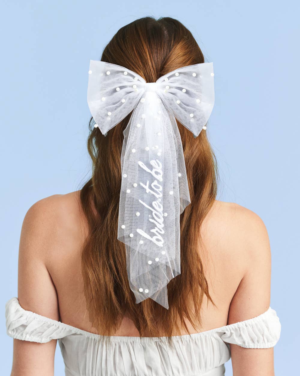 Woman wearing a large white bow in her hair with 'bride to be' text on a light blue background