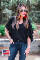 a black v-neck blouses crafted from lightweight textured fabric with asymmetrical half-flutter sleeves, front lining, and a relaxed fit, accented by a MADE IN USA watermark in the bottom left-hand corner