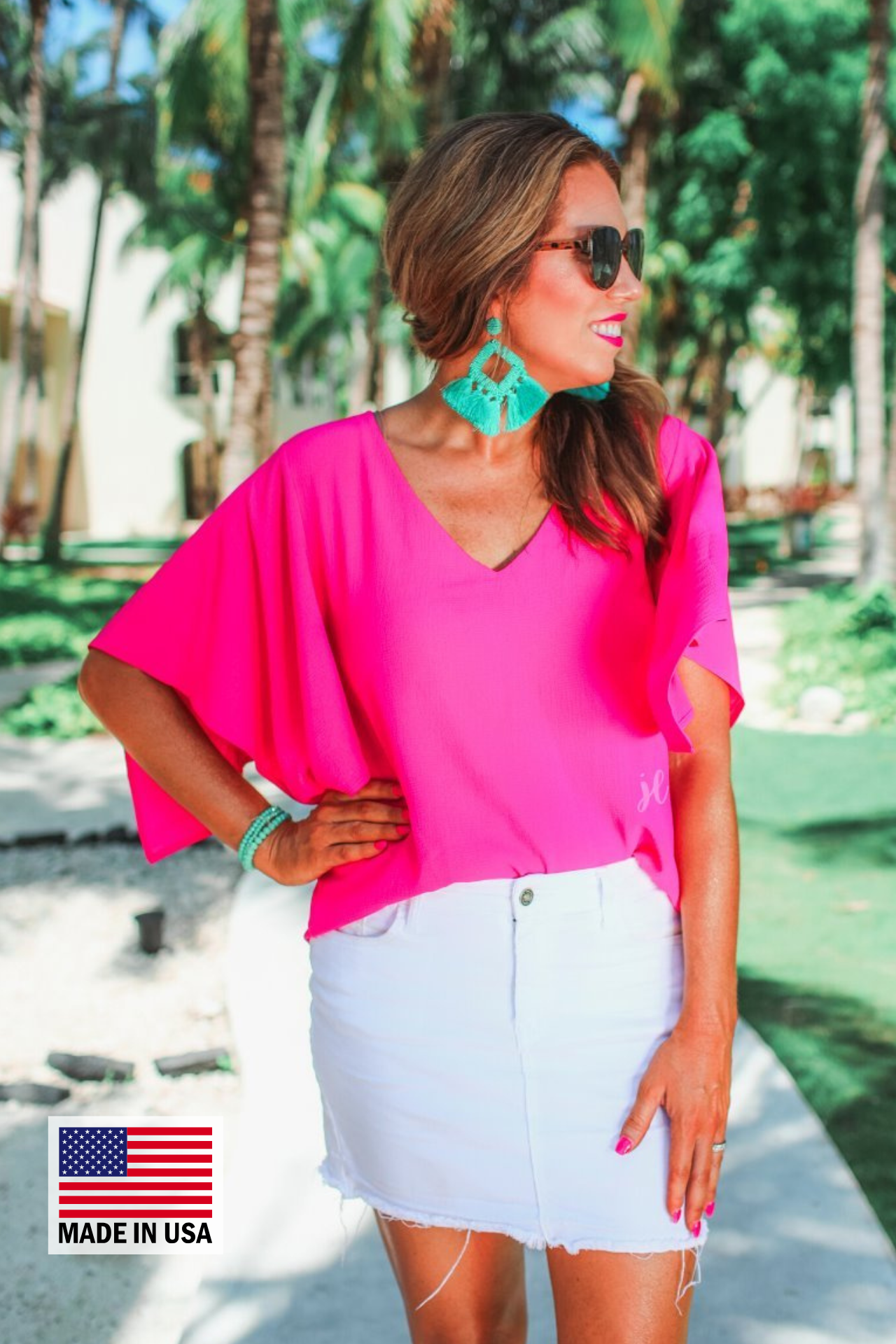 a pink v-neck blouses crafted from lightweight textured fabric with asymmetrical half-flutter sleeves, front lining, and a relaxed fit, accented by a MADE IN USA watermark in the bottom left-hand corner