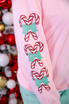 a soft pink pullover with a classic crew neckline, relaxed fit, ribbed trim, and three sparkling sequin candy cane with teal bow accents along each sleeve for a festive pop