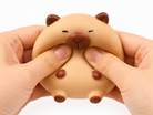 a capybara-inspired squishy toy with a rounded tan body, brown accent details, sleepy face, and smooth squeezable texture being squeezed
