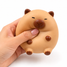 a capybara-inspired squishy toy with a rounded tan body, brown accent details, sleepy face, and smooth squeezable texture being squeezed