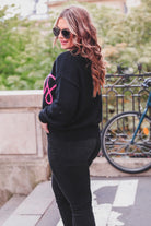 black long sleeve sweater adorned with 'cheers' in pink tinsel 