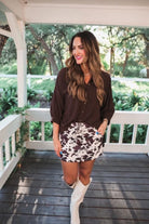mid-rise relaxed fit everyday skort made of lightweight material with built-in cream shorts, drawstring tie with gold bead accents, an elastic band on the back, and side pockets, designed on a brown cow pattern print fabric and cream base