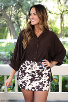 mid-rise relaxed fit everyday skort made of lightweight material with built-in cream shorts, drawstring tie with gold bead accents, an elastic band on the back, and side pockets, designed on a brown cow pattern print fabric and cream base