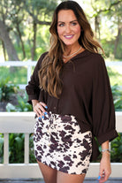 mid-rise relaxed fit everyday skort made of lightweight material with built-in cream shorts, drawstring tie with gold bead accents, an elastic band on the back, and side pockets, designed on a brown cow pattern print fabric and cream base