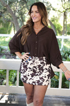 mid-rise relaxed fit everyday skort made of lightweight material with built-in cream shorts, drawstring tie with gold bead accents, an elastic band on the back, and side pockets, designed on a brown cow pattern print fabric and cream base