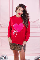 a long-sleeve pullover made from luxe material with a classic crew neckline, a relaxed drop-shoulder fit, and a statement chenille heart accented with intricate embroidery and a sequins bow-and-arrow detail