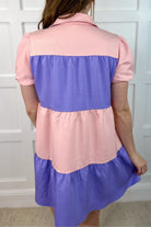a short-sleeve collared, multi-tiered button-down dress with pockets, designed in a pink and purple vertical color block stripe pattern and finished with alternating Easter bunny patch appliqués
