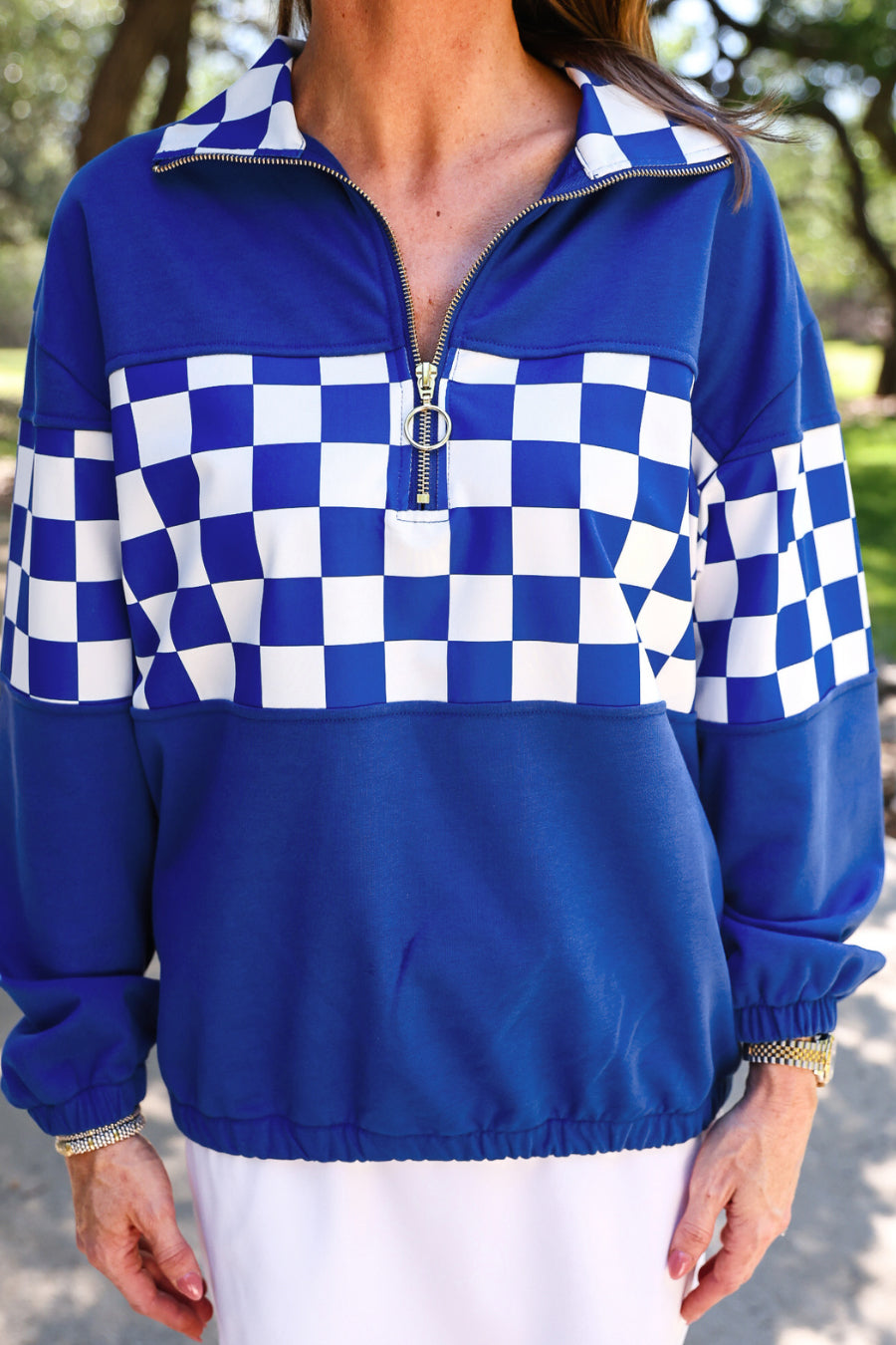 a relaxed blue half-zip pullover with gold zipper detail, checkerboard contrast panels, long sleeves, elasticized cuffs, and a softly gathered bottom hem