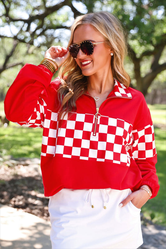 a relaxed red half-zip pullover with gold zipper detail, checkerboard contrast panels, long sleeves, elasticized cuffs, and a softly gathered bottom hem