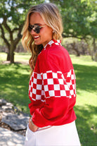 a relaxed red half-zip pullover with gold zipper detail, checkerboard contrast panels, long sleeves, elasticized cuffs, and a softly gathered bottom hem