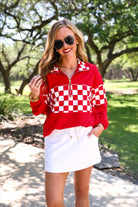 a relaxed red half-zip pullover with gold zipper detail, checkerboard contrast panels, long sleeves, elasticized cuffs, and a softly gathered bottom hem