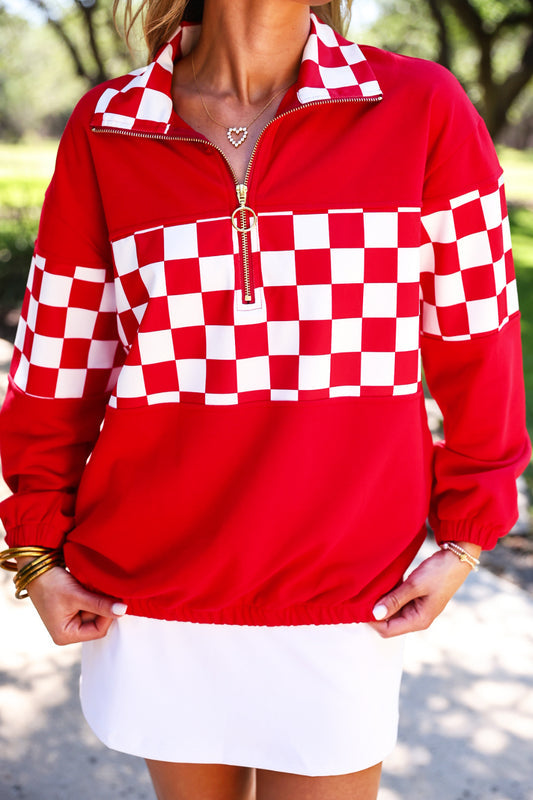 a relaxed red half-zip pullover with gold zipper detail, checkerboard contrast panels, long sleeves, elasticized cuffs, and a softly gathered bottom hem