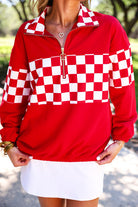 a relaxed red half-zip pullover with gold zipper detail, checkerboard contrast panels, long sleeves, elasticized cuffs, and a softly gathered bottom hem