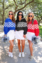 a relaxed half-zip pullover with gold zipper detail, checkerboard contrast panels, long sleeves, elasticized cuffs, and a softly gathered bottom hem in black, blue, and red