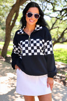 a relaxed black half-zip pullover with gold zipper detail, checkerboard contrast panels, long sleeves, elasticized cuffs, and a softly gathered bottom hem