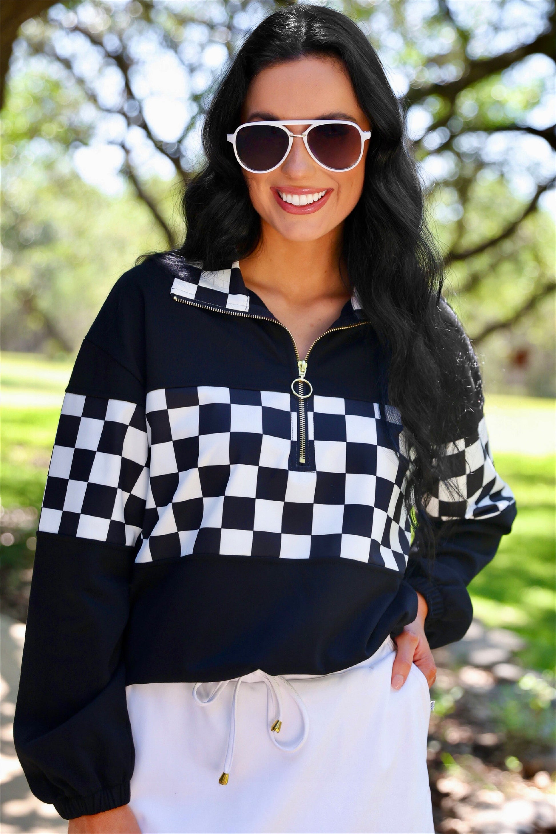a relaxed black half-zip pullover with gold zipper detail, checkerboard contrast panels, long sleeves, elasticized cuffs, and a softly gathered bottom hem