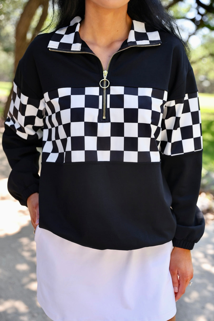 a relaxed black half-zip pullover with gold zipper detail, checkerboard contrast panels, long sleeves, elasticized cuffs, and a softly gathered bottom hem