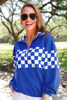 a relaxed blue half-zip pullover with gold zipper detail, checkerboard contrast panels, long sleeves, elasticized cuffs, and a softly gathered bottom hem